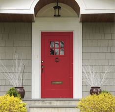 a red front door with two planters on the steps and bushes in front of it