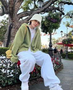 a person sitting on a bench wearing white pants and a green jacket with hoodie