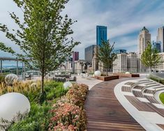 a wooden walkway with benches and plants in the foreground, overlooking a cityscape