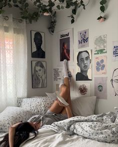 a woman laying on top of a bed next to a wall covered in pictures and plants