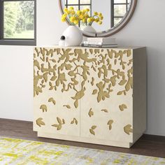 a white and gold cabinet with yellow flowers on the top, in front of a round mirror