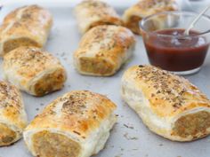 several sausage rolls on a baking sheet with ketchup in a small glass dish