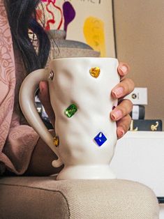 a woman is holding a coffee cup with different colored jewels on it's side