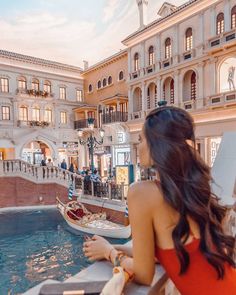 a woman in an orange dress sitting on a ledge looking at the water and buildings