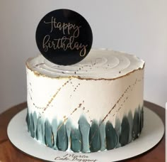 a white and blue cake with a happy birthday sign on top, sitting on a wooden table