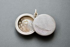 Poetic and beautiful locket, holding a secret message stamped on small letter plates, a feather and a little golden heart. The lid of the locket is decorated with a delicate feather. You can open the locket by sliding the lid to the side.  Glass-Locket  - diameter 22mm (0,86") - thickness: ca. 6mm (0,24") - design: feather - Sterling Silver - filled with silver plates, stamped with letters, a feather and a golden heart How it works: * The lockets consist of two movable parts, fitting tightly tog Engraved Amulet Locket Necklace As Gift, Silver Amulet Jewelry With Locket, Oval Silver Locket Necklace In Brass, Silver Oval Locket Necklace In Brass, Silver Engraved Amulet Locket Necklace, Secret Message Locket, Puzzle Ring, Golden Heart, Glass Locket