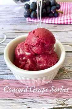 a bowl filled with red ice cream next to grapes