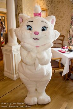 a large white cat mascot standing in the middle of a room with tables and chairs