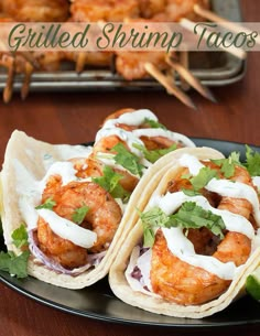 three shrimp tacos on a black plate with cilantro and sour cream sauce