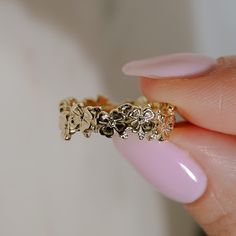 a close up of a person's hand holding a gold ring with flowers on it