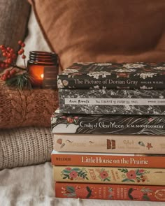 a stack of books sitting on top of a bed next to a cup and candle