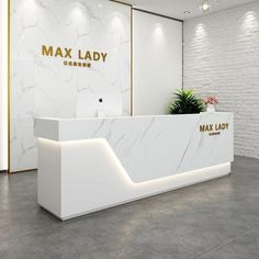 a white marble reception desk with gold lettering on the front and side panels that read max lady