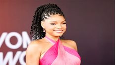 a woman in a pink dress smiling at the camera with her hair pulled back and braided