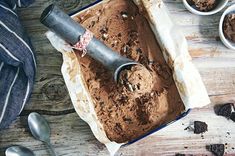 a pan filled with chocolate ice cream next to bowls of cookies and spoons on a wooden table