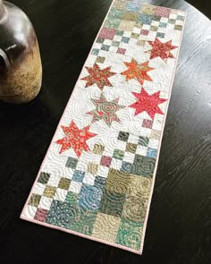 a quilted table runner sitting on top of a wooden table next to a vase