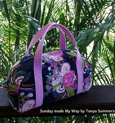 a blue floral bag with pink straps sitting on top of a wooden table next to palm trees