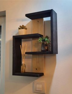 two wooden shelves with plants and candles in them on the wall next to a light switch