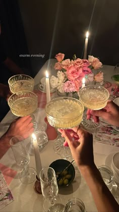 people are toasting at a table with wine glasses and flowers in the center, surrounded by candles