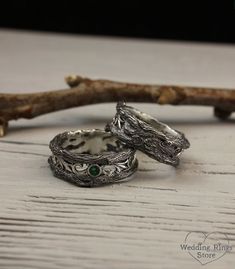 two silver rings with green stones sitting on top of a wooden table next to a twig