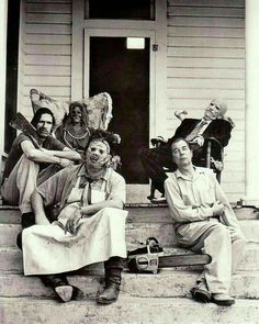 an old black and white photo of four people sitting on the front steps of a house