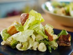 a salad with lettuce and bacon is on a blue plate next to a bowl