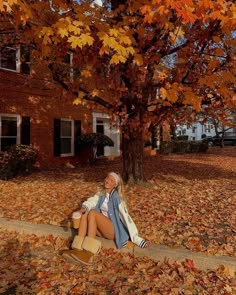 a woman sitting on the ground in front of a tree with leaves all over it