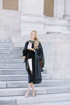 a woman standing in front of some steps wearing a black coat and white dress with heels