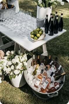 a table with wine glasses and bottles on it in the grass next to some flowers