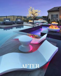 an outdoor lounge area next to a swimming pool at night with lights on the water