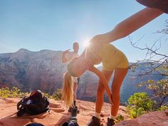 two people standing on top of a mountain with their feet in the air and one person leaning over