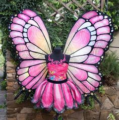 a pink and black butterfly costume on display in front of a stone wall with trees