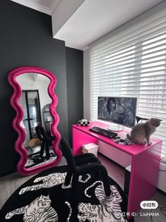 a cat sitting on top of a pink desk in front of a mirror and dresser