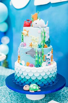 a three tiered cake decorated with sea animals and under the sea theme is on a blue plate