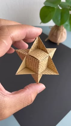 a hand holding an origami star on top of a table next to a potted plant