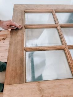 a person is working on a window frame with wood and glass inserts in place