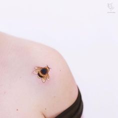 a small bee tattoo on the back of a woman's left shoulder and chest