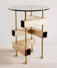 a glass table with gold metal legs and shelves on each side that are stacked up against the wall