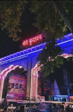 the entrance to an event lit up in blue and pink lights at night with cars parked outside