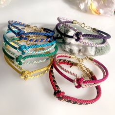 four different colored bracelets on a white surface with flowers in the backgroud