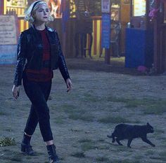 a woman walking next to a black cat