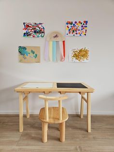 a wooden table with two chairs in front of it and paintings on the wall behind it