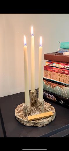 three candles are lit on a table next to some books and a pencil in a bowl