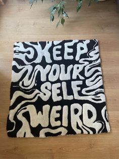 a black and white rug with the words sleep your self weird printed on it, in front of a potted plant