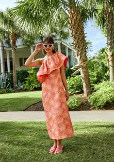 a woman standing in the grass wearing sunglasses and a dress with ruffles on it