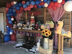 an outdoor party with balloons and decorations on the wall, hay bales in front of it