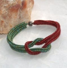 a red and green beaded bracelet next to a piece of bread