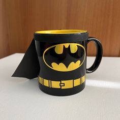 a batman coffee mug with a black and yellow batman logo on the inside is sitting on a white surface