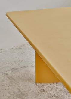 a yellow table sitting on top of a cement floor next to a white wall in an empty room