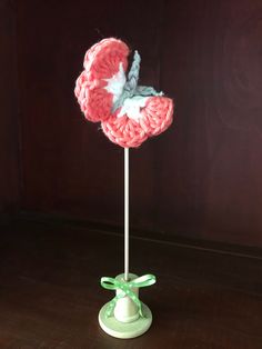 a pink and white crocheted flower on top of a green stand with a bow