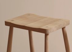 a wooden stool with two legs and a square seat on the bottom, in front of a beige wall